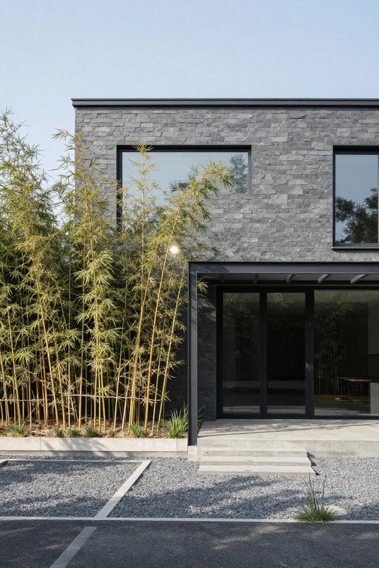 Modern gray stone house with large windows and bamboo garden.