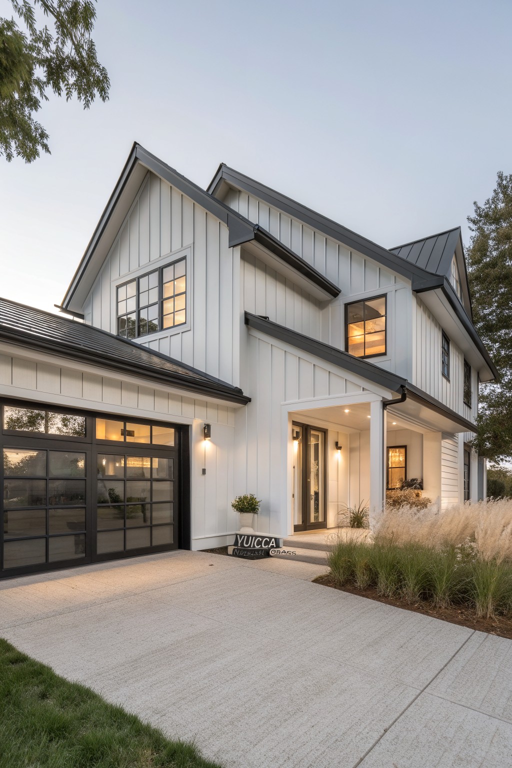Modern farmhouse house exterior featuring white board-and-batten siding, black metal roof, black-framed windows and garage door, covered entry porch, and ornamental grasses along the front driveway.