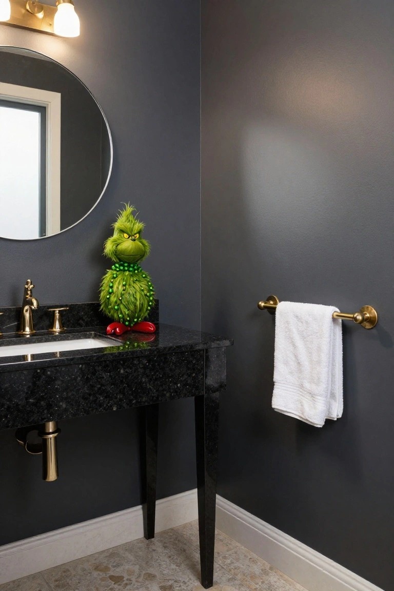 Bathroom vanity with black granite countertop holding a green Grinch plush figure next to gold faucet and handles, white towel on gold towel bar, round mirror on dark gray wall, and gold sconce light.