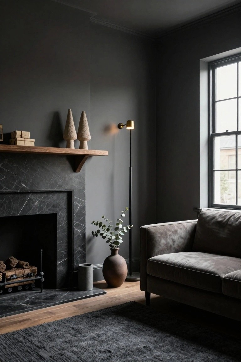Dark gray living room corner with black marble fireplace, wooden mantel shelf holding two asymmetrical textured pine trees and small wood boxes, tall floor lamp, gray velvet sofa, eucalyptus in terracotta pot, and dark rug on oak floors.