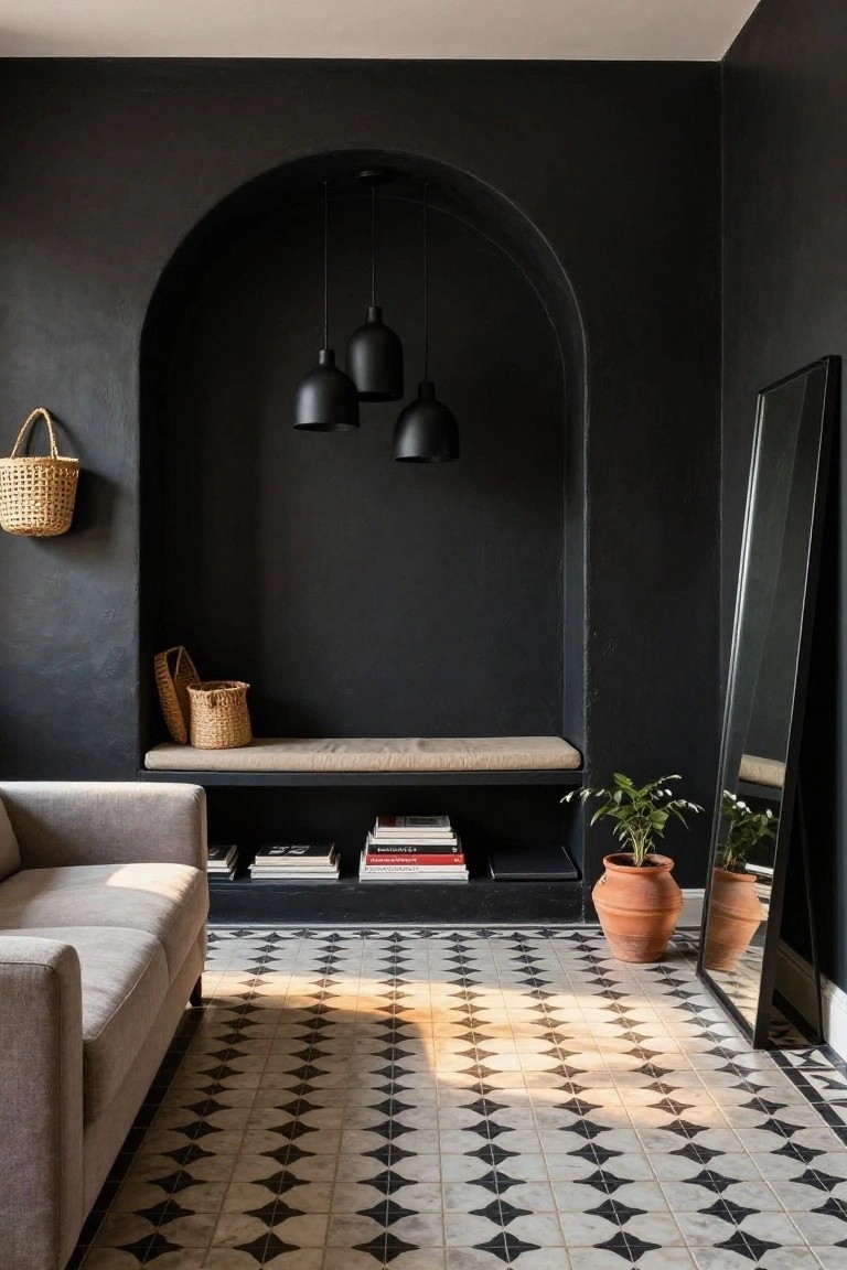 A living room with black textured walls, an arched niche containing black pendant lights, a cushioned bench with woven baskets and books, a gray sofa, terracotta pots with plants, a full-length black-framed mirror, and black-and-white diamond-patterned floor tiles.