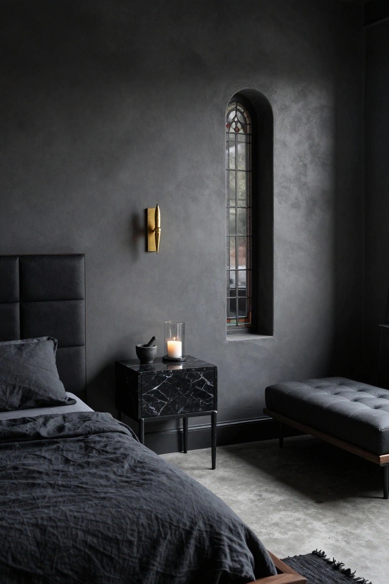 Dark textured bedroom with black tufted headboard bed, black marble nightstand holding glass cloche candle and stone mortar pestle, gold wall sconce, tall arched stained glass window, and black bench.