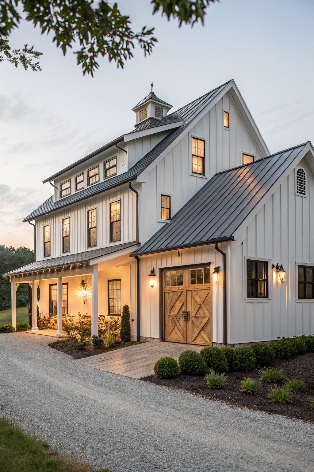 A white two-story barndominium with vertical siding, a dark metal roof, cupola, and a large wooden barn-style double door centered on the front facade.