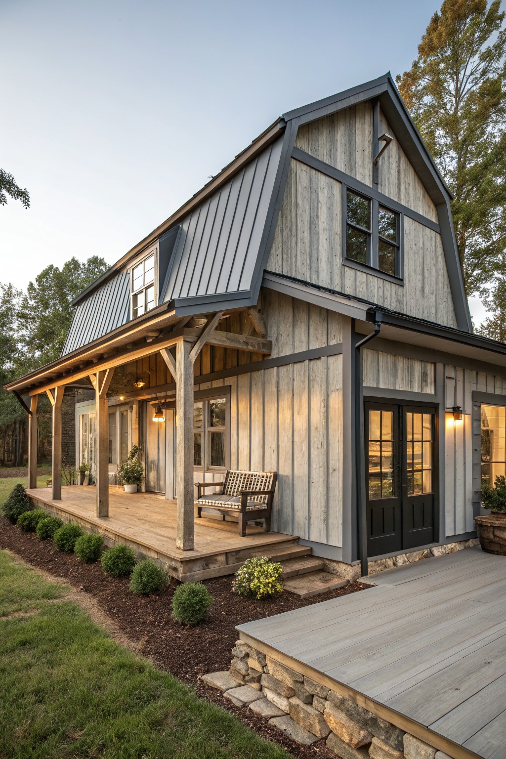 Modern gray barn home with porch bench, black doors, wooden deck, and stone foundation.