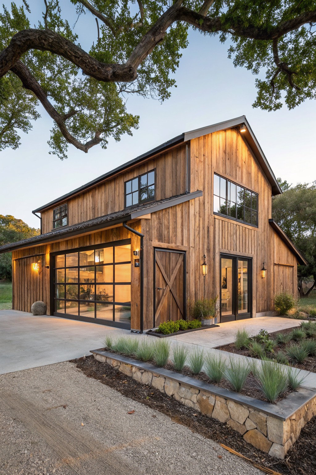 Modern wooden barn house with large windows, stone landscaping, and evening lights