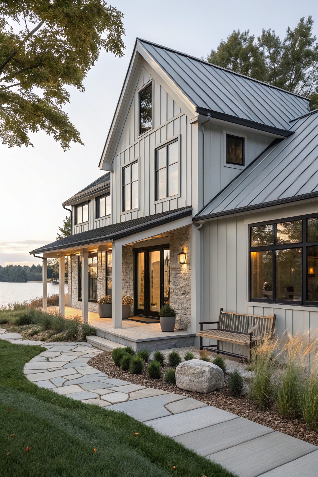 Modern farmhouse with light blue siding, metal roof, and porch overlooking a lake.