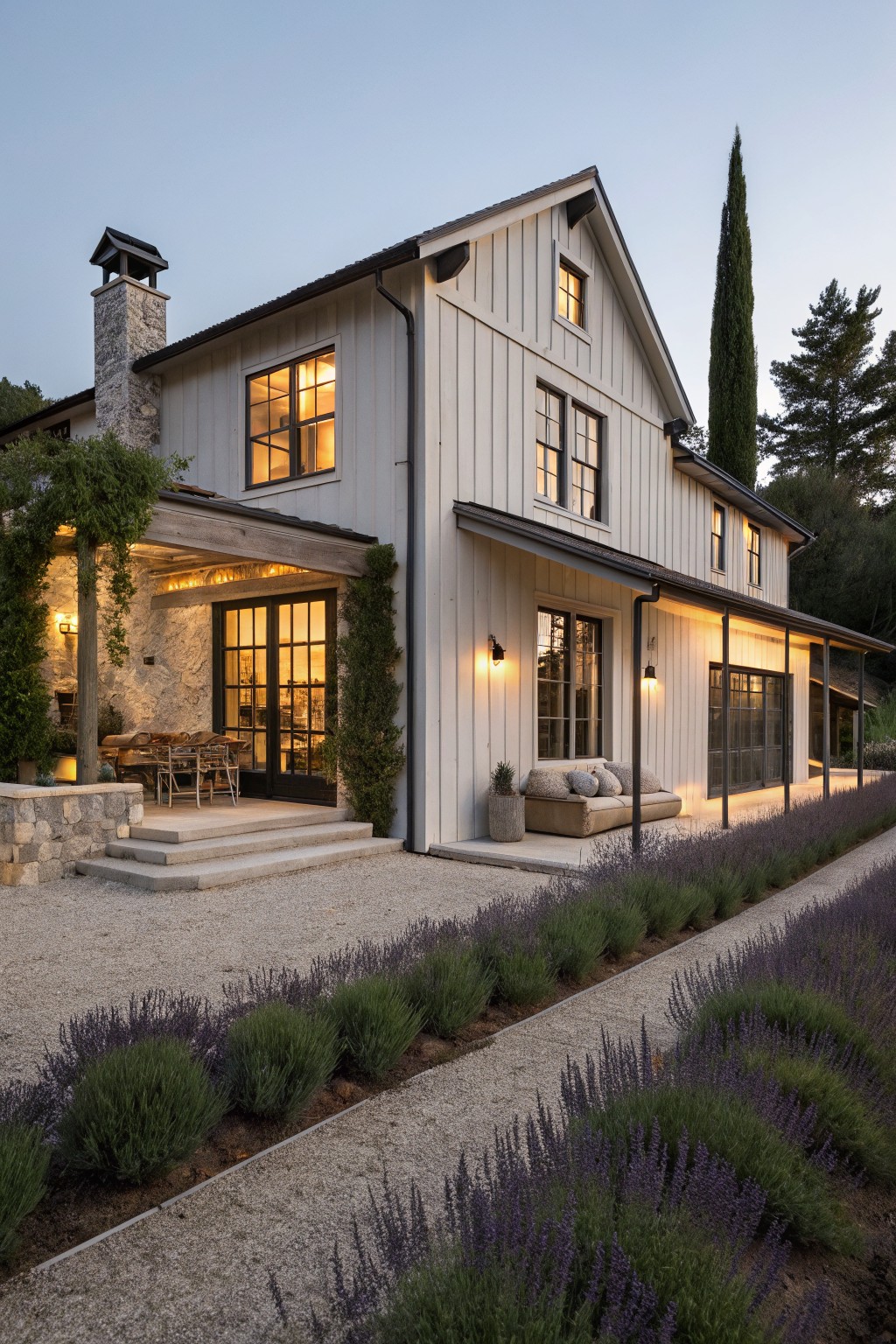 White farmhouse with stone chimney, black windows, and lavender garden at dusk