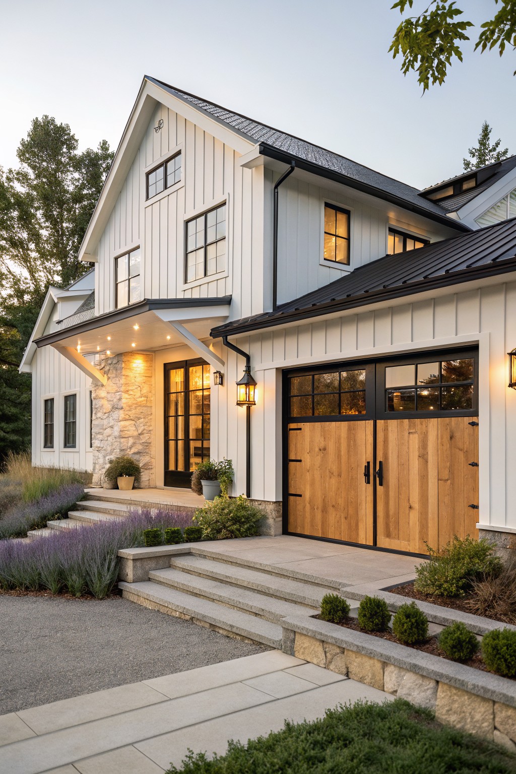 A two-story white farmhouse exterior with vertical siding, a stone entry wall, black-framed windows and doors, and large wooden garage doors.