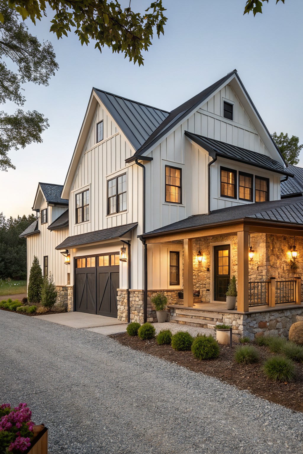 A two-story modern farmhouse with white vertical siding, dark metal roof, stone on the porch and garage base, and a gravel driveway in front.