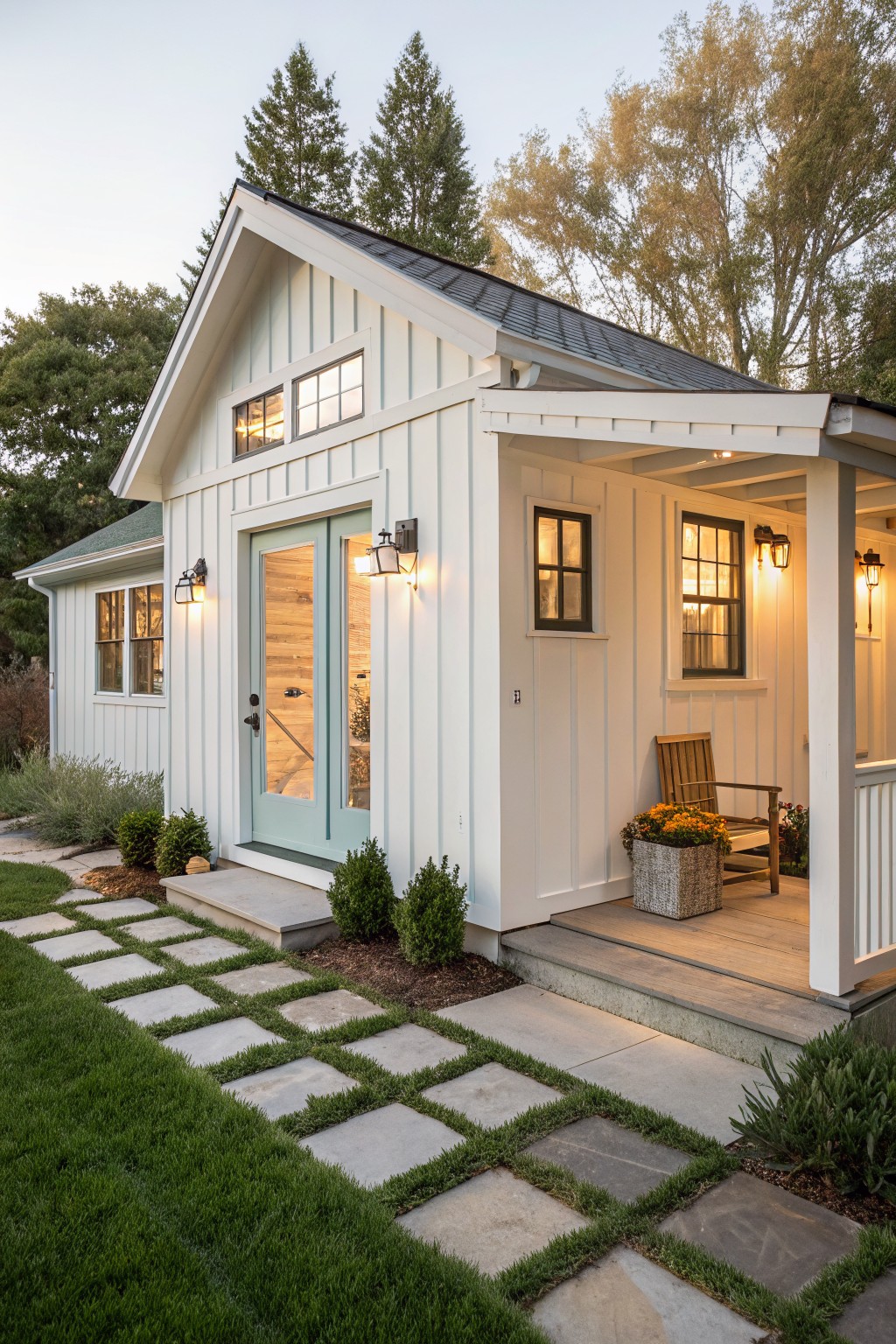 A small white farmhouse exterior with vertical siding, a light blue front door, black roof, covered porch, and a stone pathway leading to the entrance.