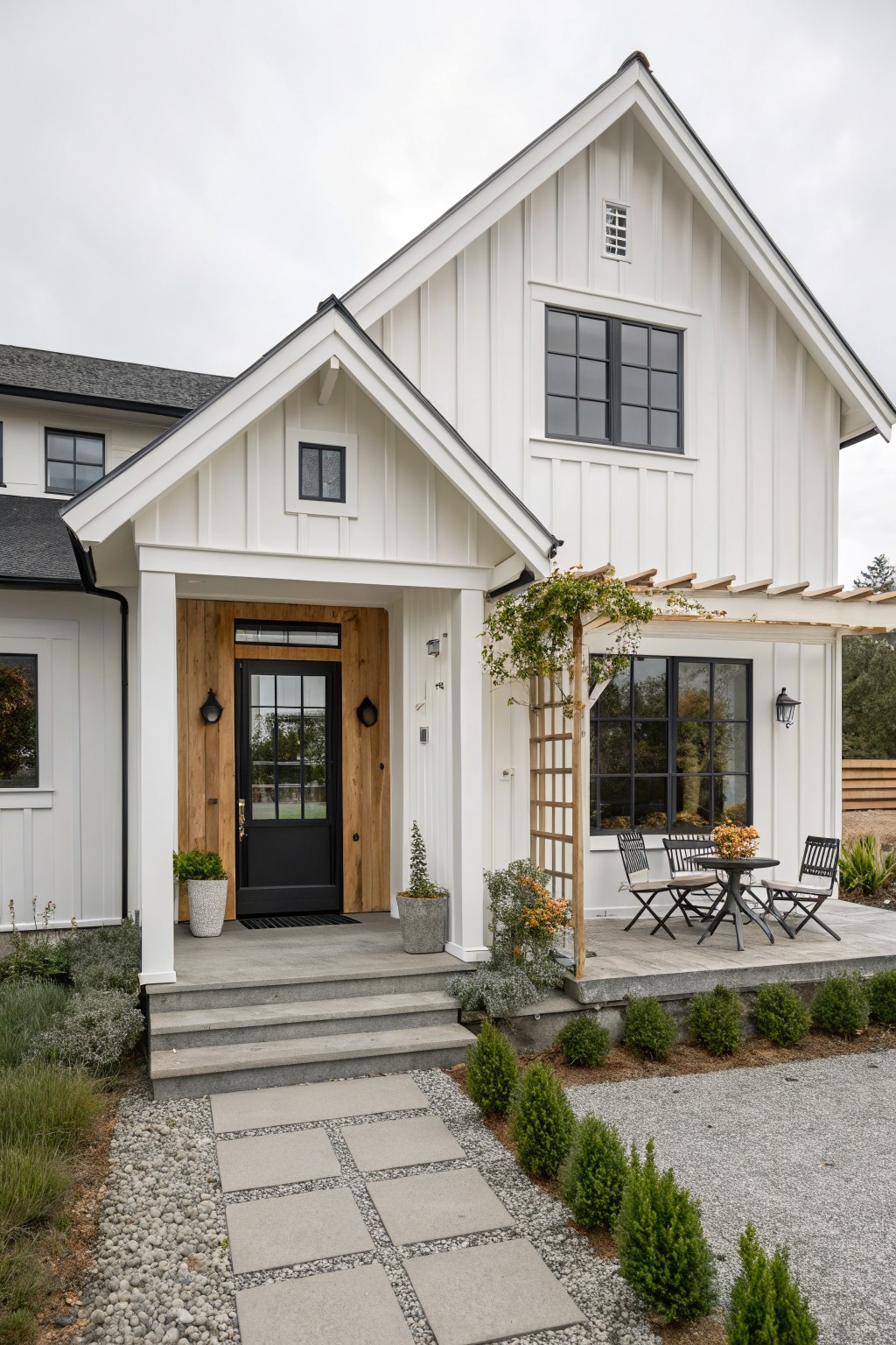 Front view of a compact white farmhouse with vertical siding, a black door set in wood trim, and a small covered porch.