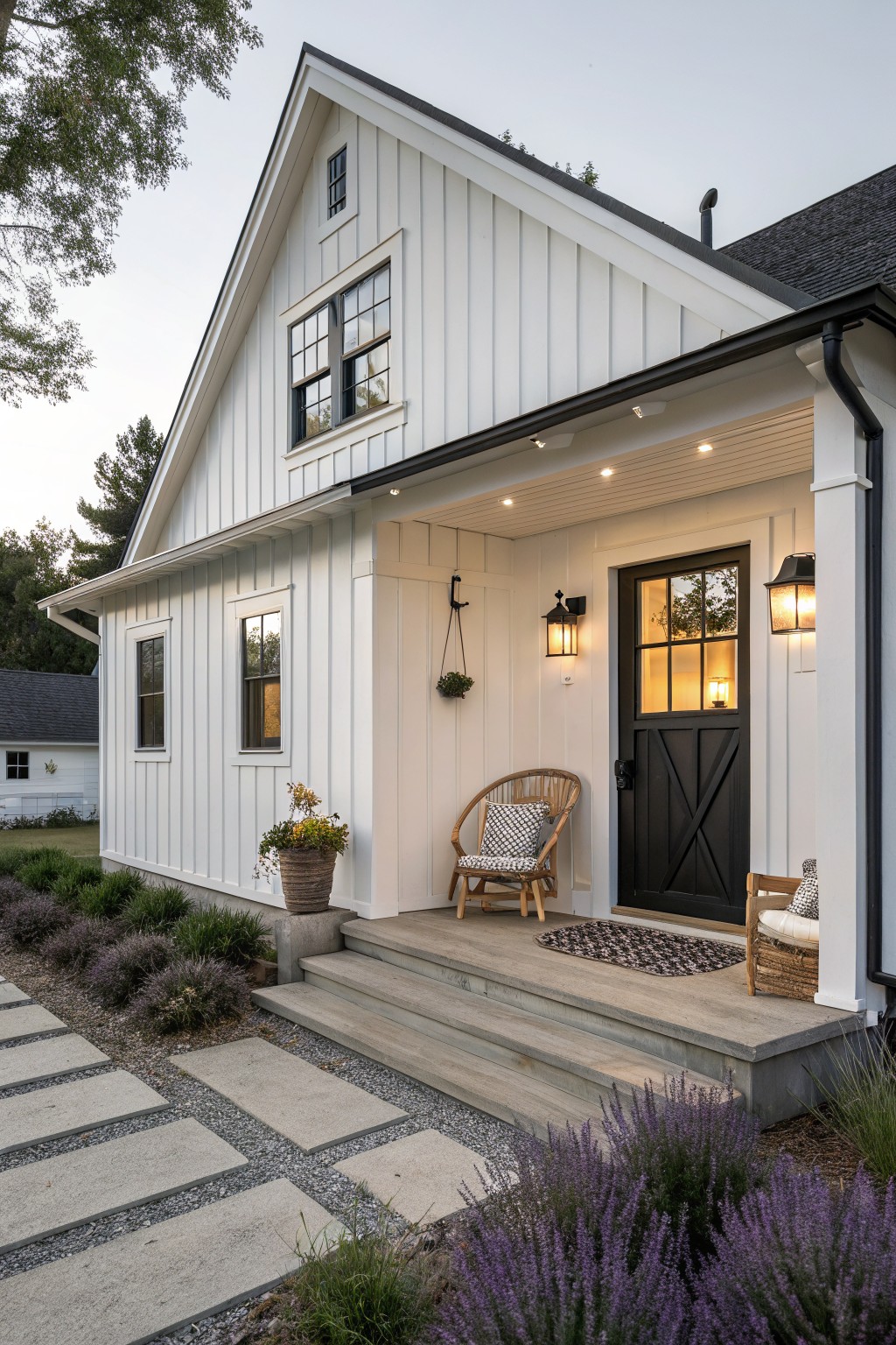 A small white farmhouse with vertical siding, a black front door on a covered porch, and concrete steps leading up from a stone path.