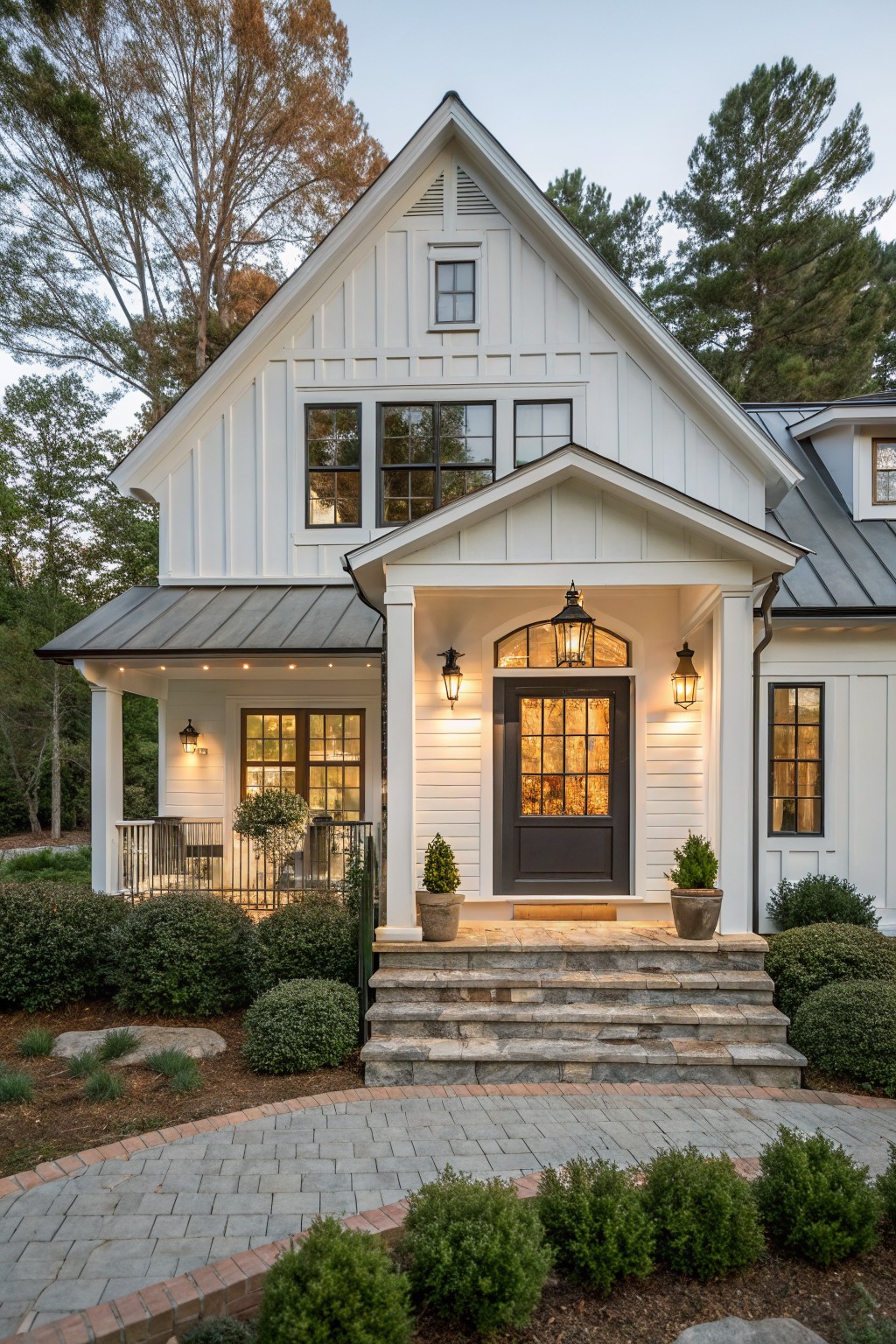 A small white farmhouse with a dark front door centered under a gabled porch, stone steps, and black lanterns on either side.