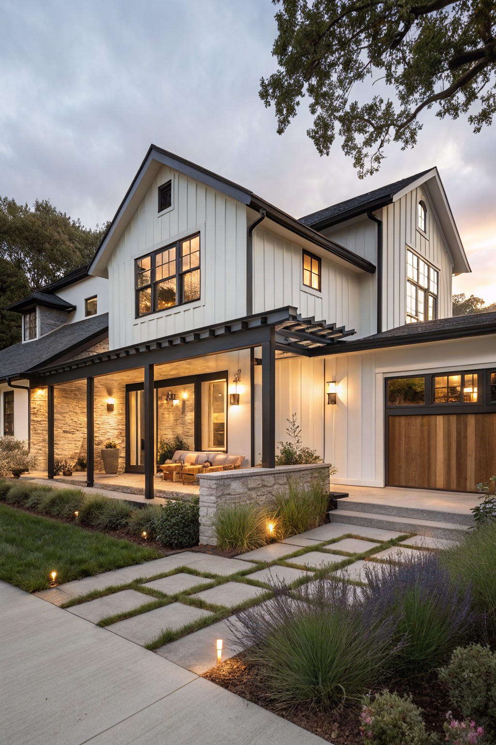 A modern farmhouse with white vertical siding, a dark-framed covered porch, stone accents on the base, and a concrete paver walkway leading to the front.