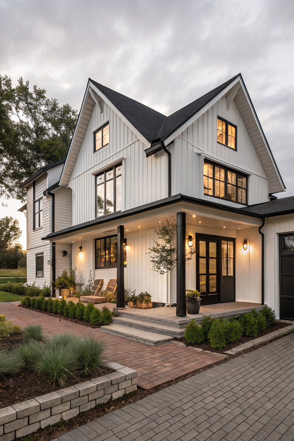 A white modern farmhouse with black trim, black-framed windows and door, a covered porch with black columns, and surrounding landscaping with brick pathways.