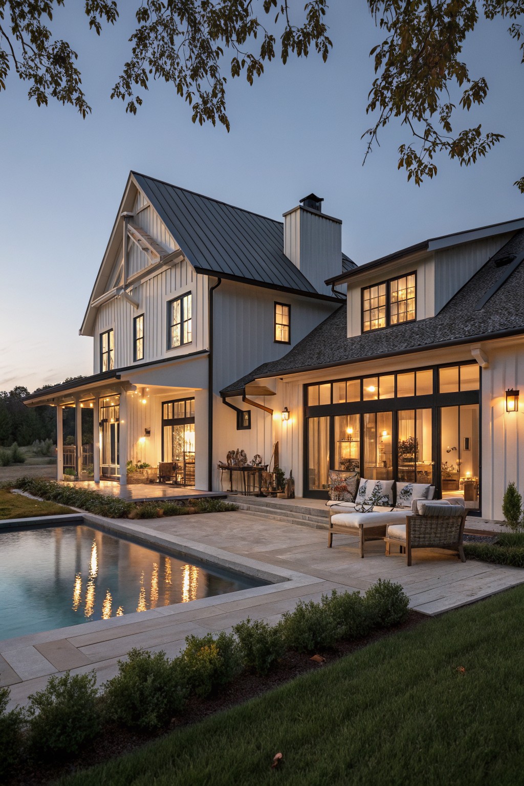 Modern farmhouse with white board and batten siding, a dark metal roof, black window frames, and a pool with patio seating in the foreground.