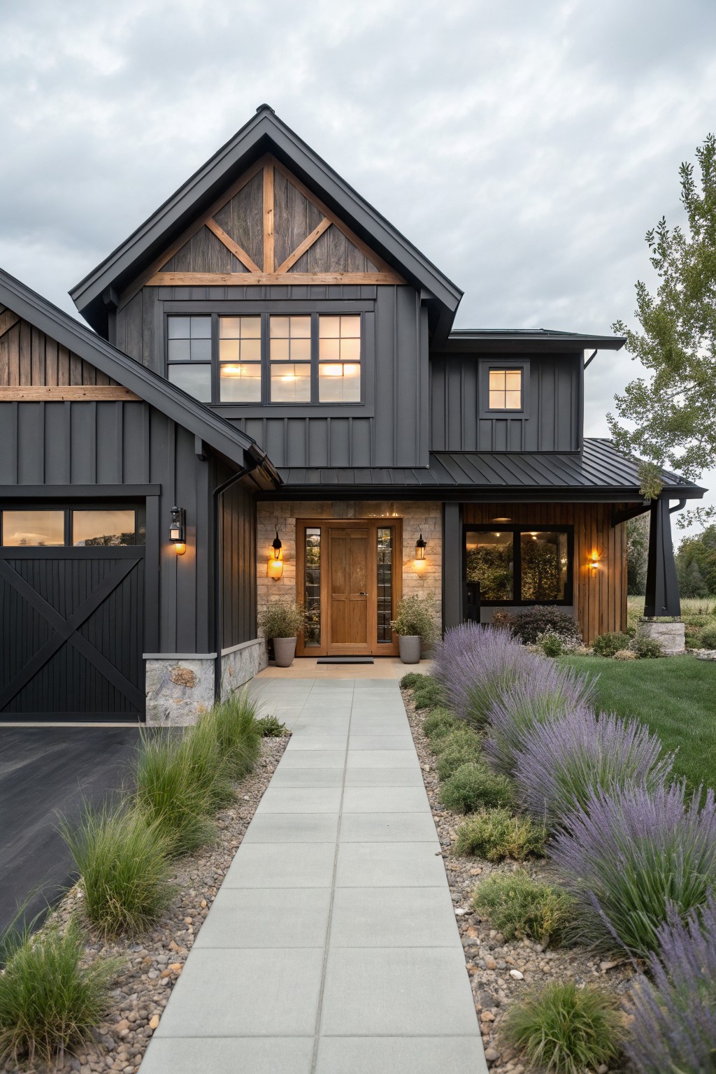 A modern farmhouse exterior with dark siding, a prominent front gable featuring exposed wooden timber framing in an X pattern, a central wooden door, and a concrete walkway.