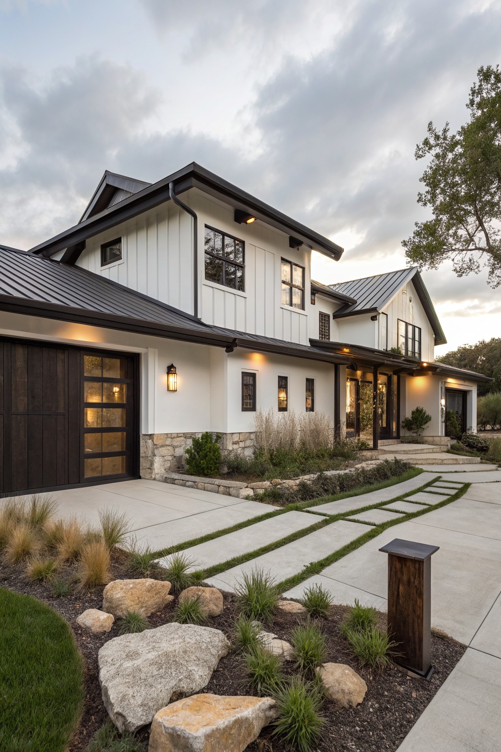 A two-story modern farmhouse with white vertical siding, dark metal roofing, a stone foundation, and a dark wood garage door on the left side.