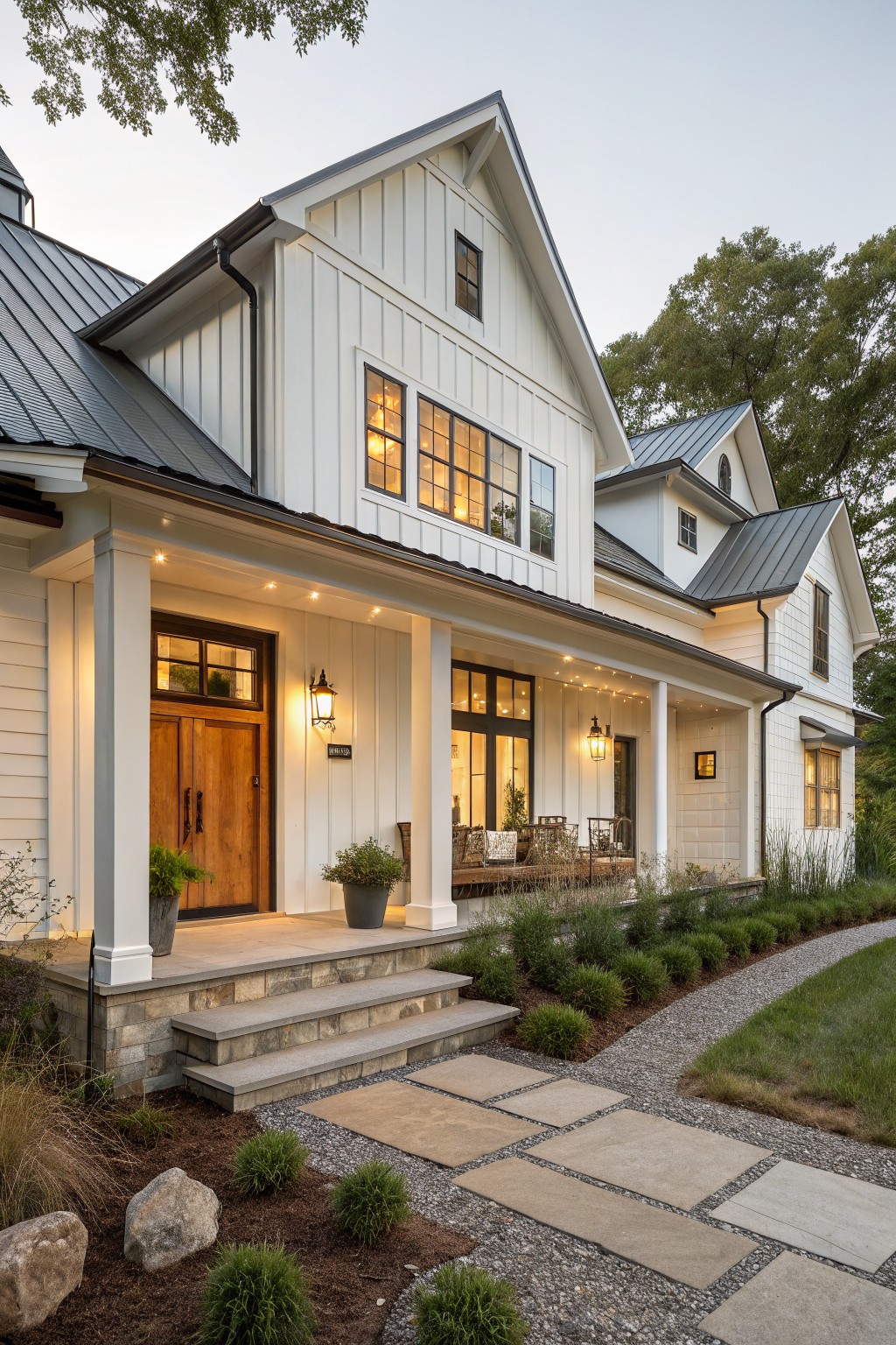 A white modern farmhouse exterior with vertical siding, black-framed windows, a dark metal roof, a covered porch with white columns, and stone steps leading to a wooden front door.