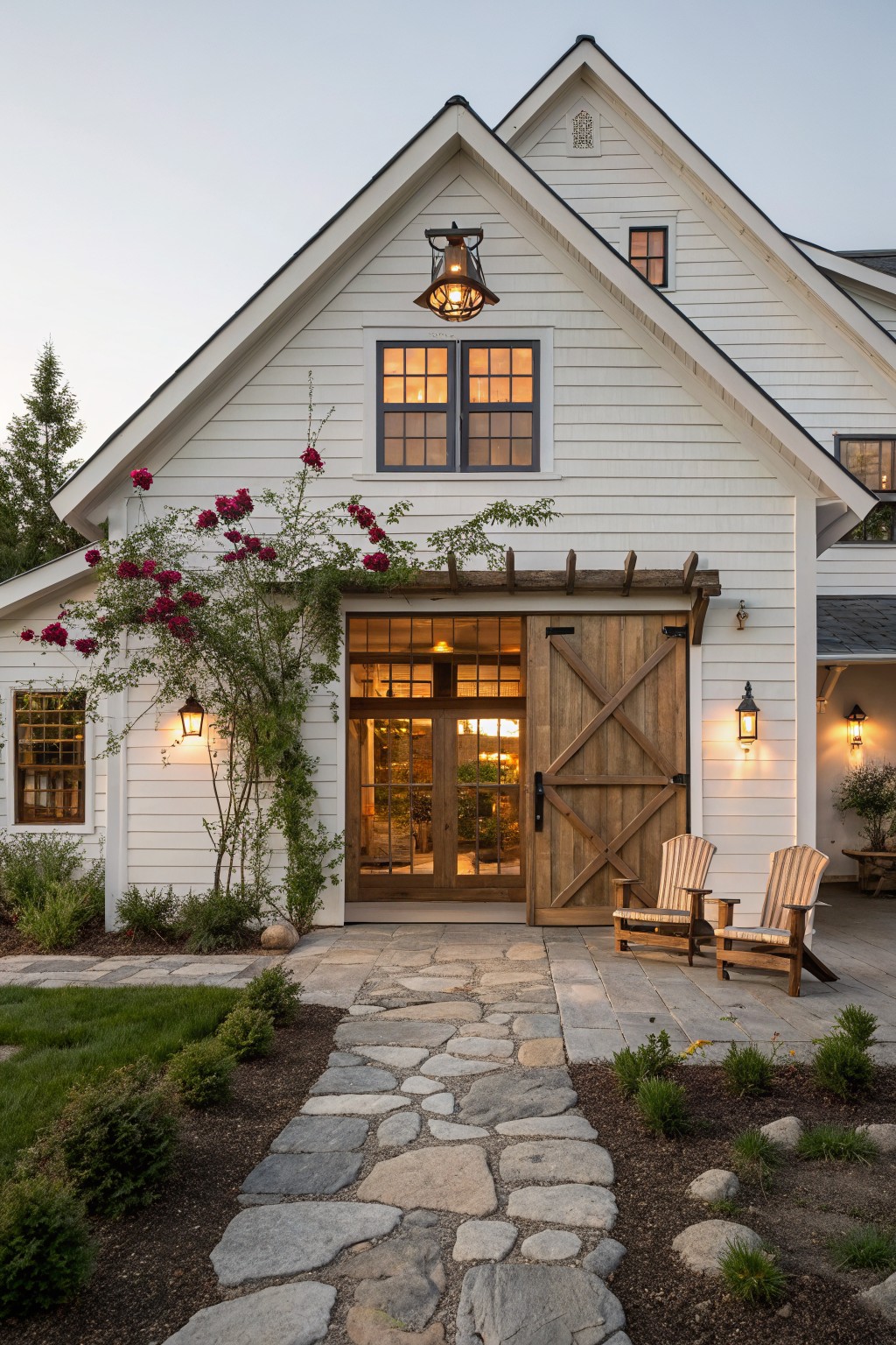 A white farmhouse exterior featuring a large wooden barn-style door, double windows above it, a stone pathway leading to the entrance, and rose vines growing along the left side.