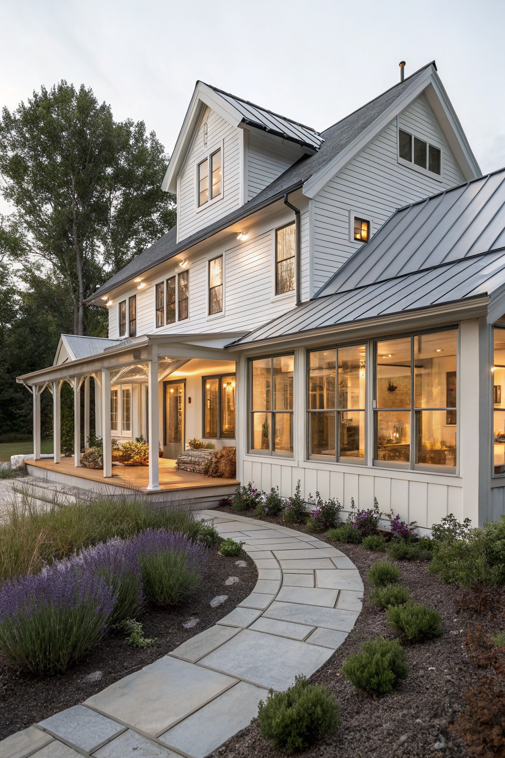 Two-story white farmhouse with lit porch, stone path, and purple garden at dusk