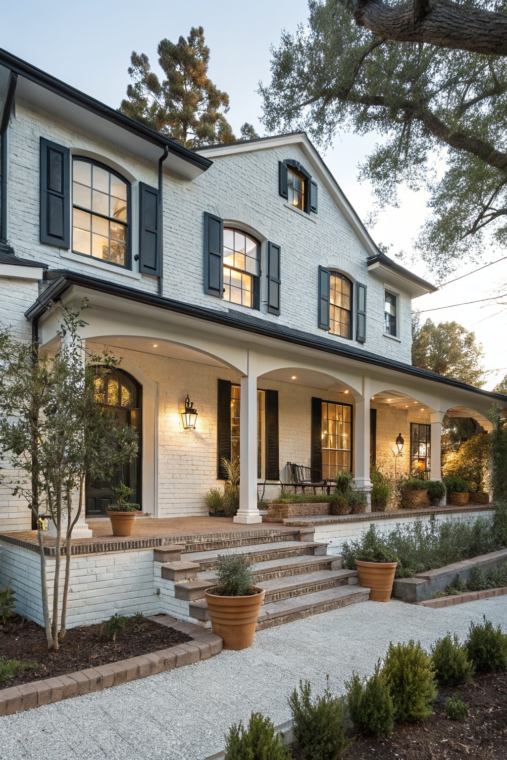 White brick house with black shutters, arched porch, steps, and potted plants.