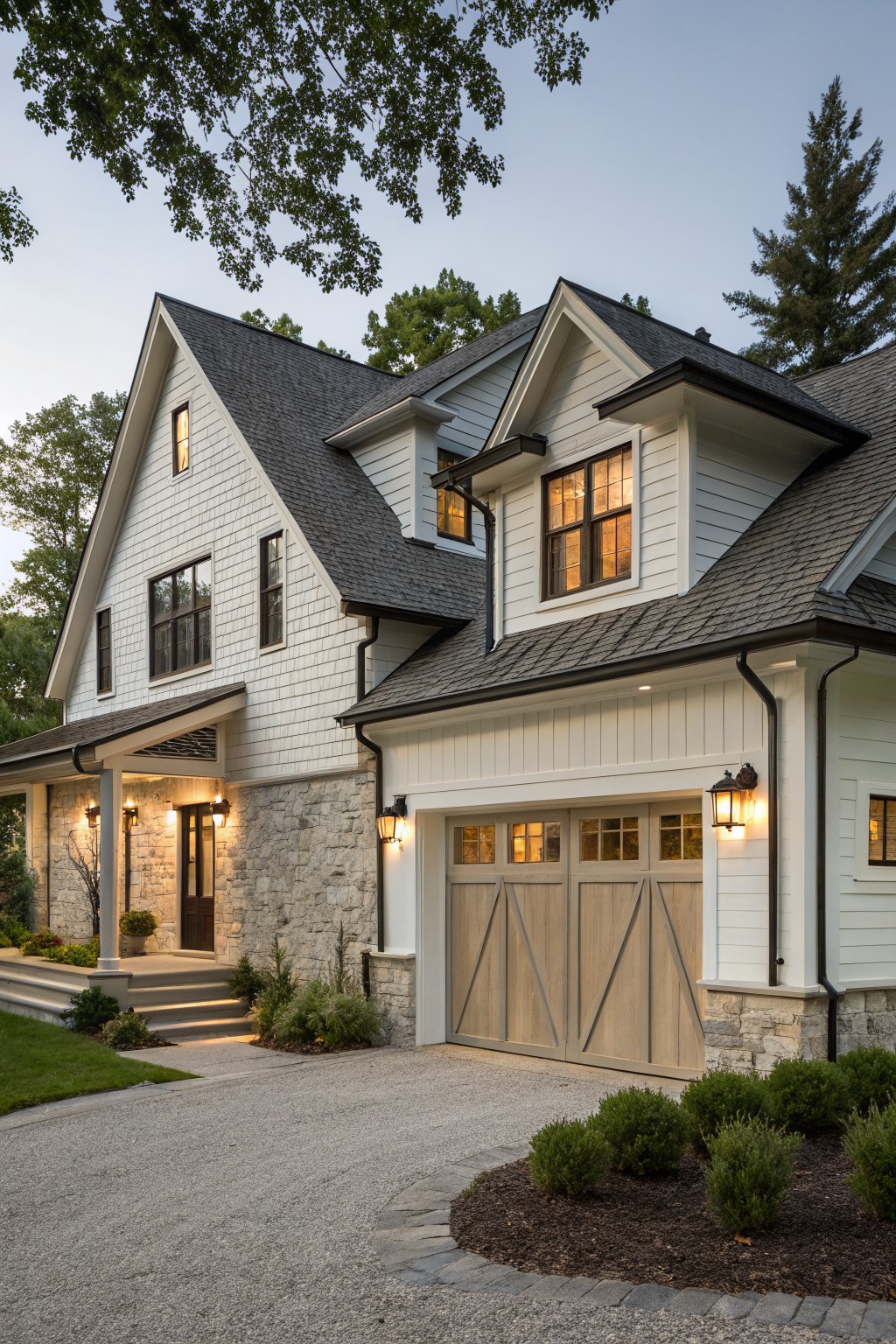 White farmhouse exterior with an attached two-car garage featuring light wood doors, white siding, and a stone foundation.