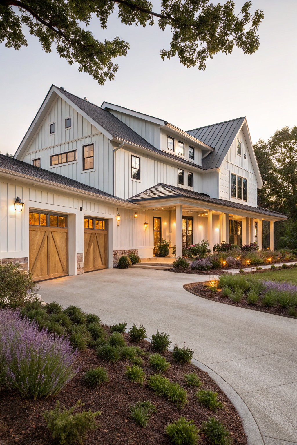 A white two-story farmhouse with wooden garage doors on the left, a covered front porch with columns, and landscaping along a curved concrete driveway.