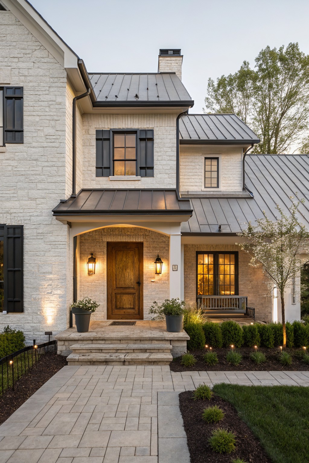 Stone house with wooden door, lit lanterns, steps, and landscaped garden at dusk