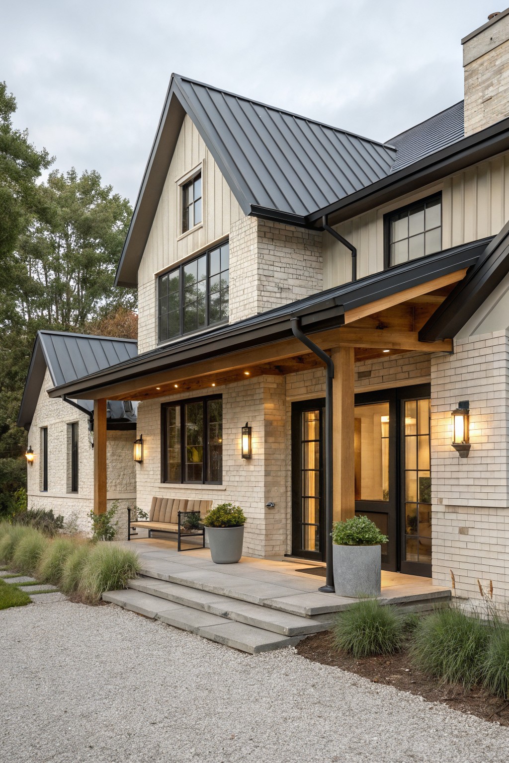 A coastal farmhouse exterior with a dark metal roof, natural wood porch supports, white brick and siding, and a covered entry with black-framed doors.