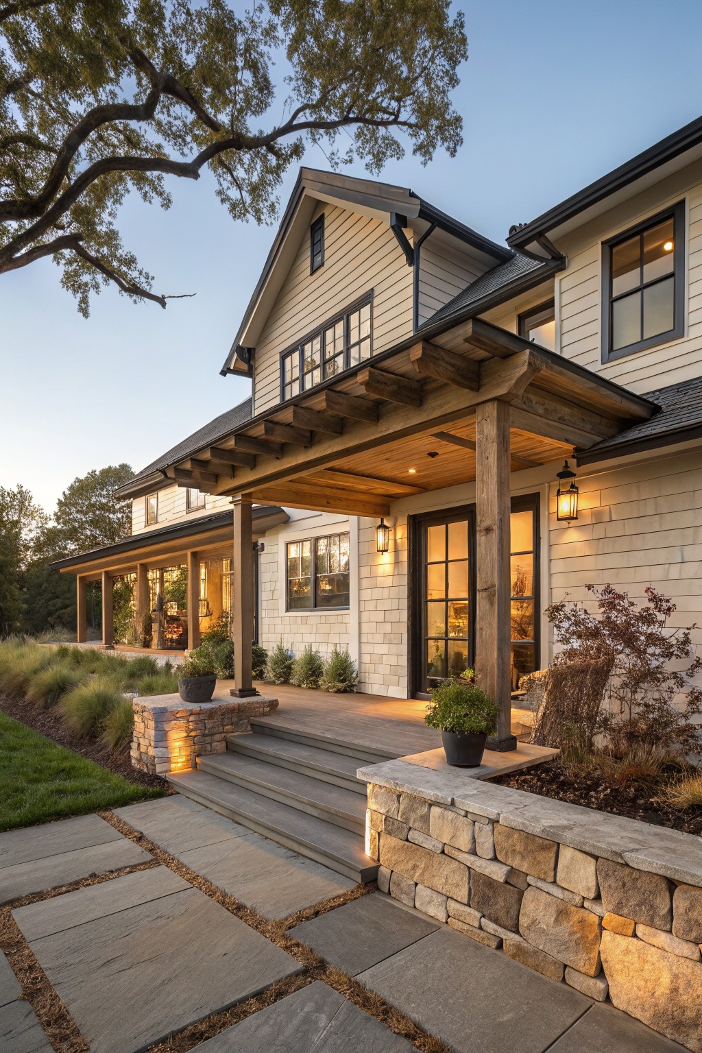 A farmhouse exterior with light siding, a covered wooden porch supported by thick timber beams and posts, stone steps, and landscaping at dusk.