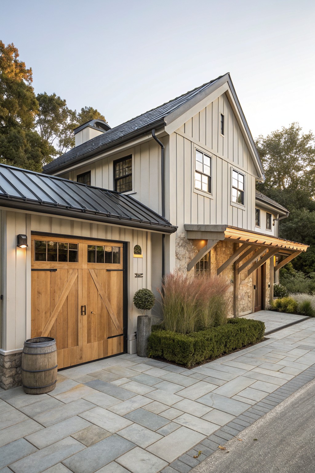 A two-story farmhouse exterior with light siding, a large wooden garage door, stone accents around the entry, and a paved driveway with landscaping.
