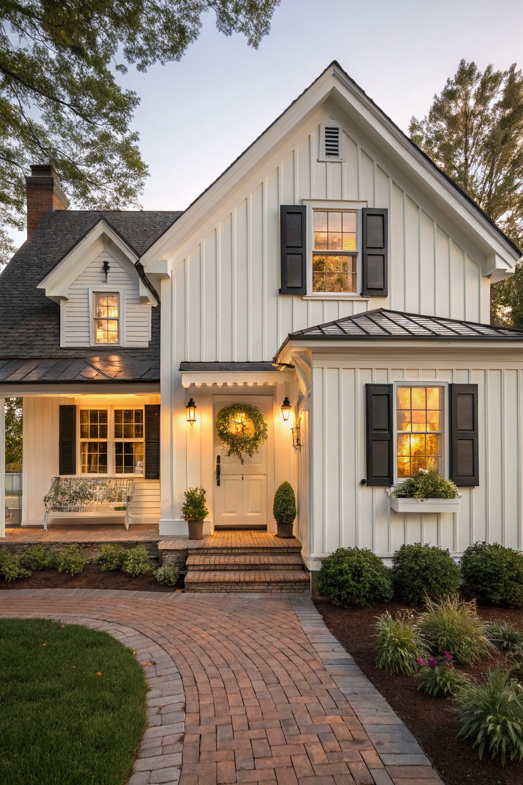 A white two-story farmhouse with black shutters on multiple windows, a front door with a wreath, and a brick path leading to the steps.
