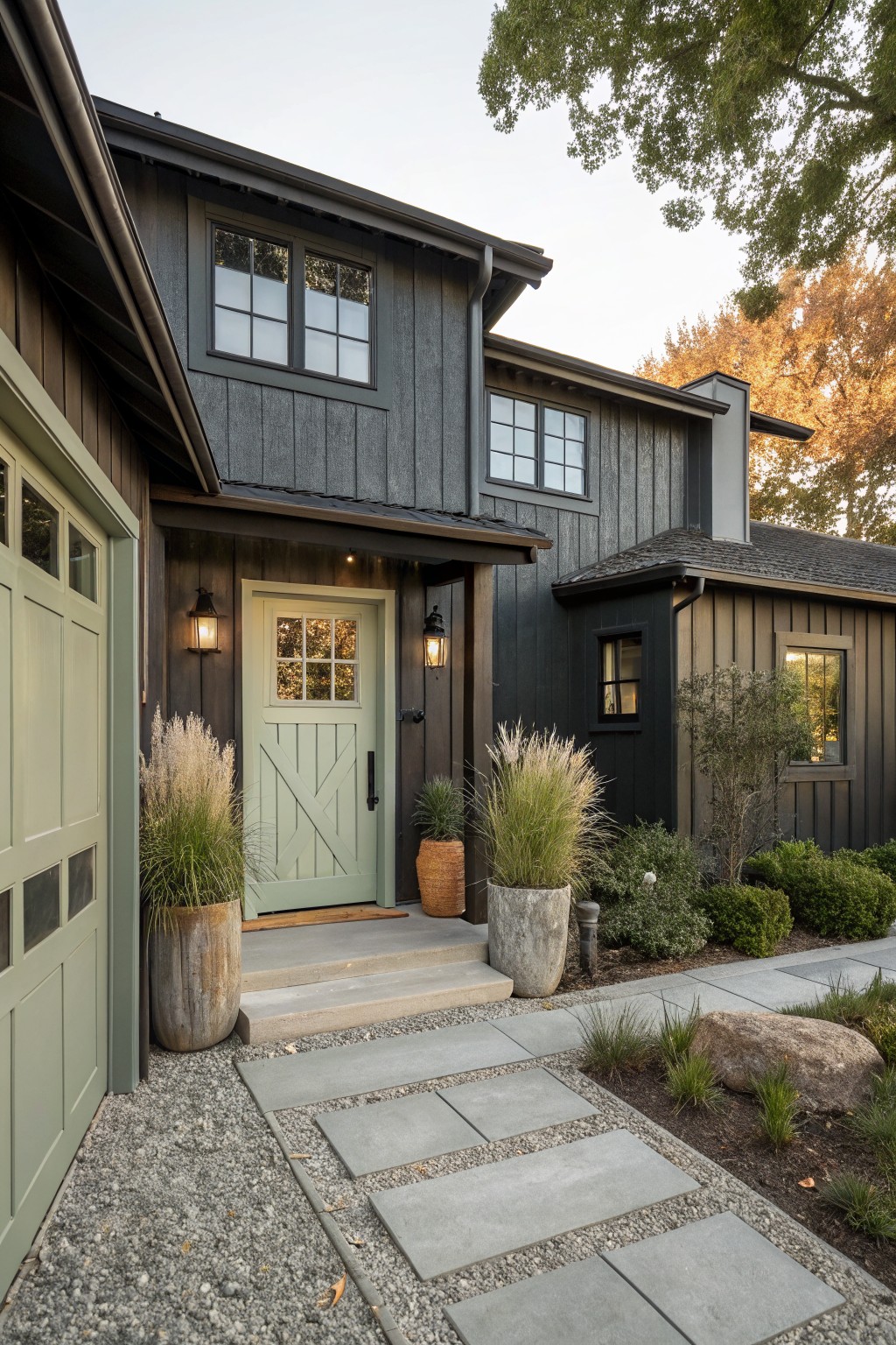 Front view of a dark gray house exterior showing a light green door, concrete steps, potted plants, and a stepping stone path on gravel.