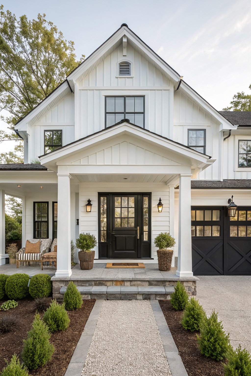 White two-story house with black door, garage, porch columns, and gravel path.