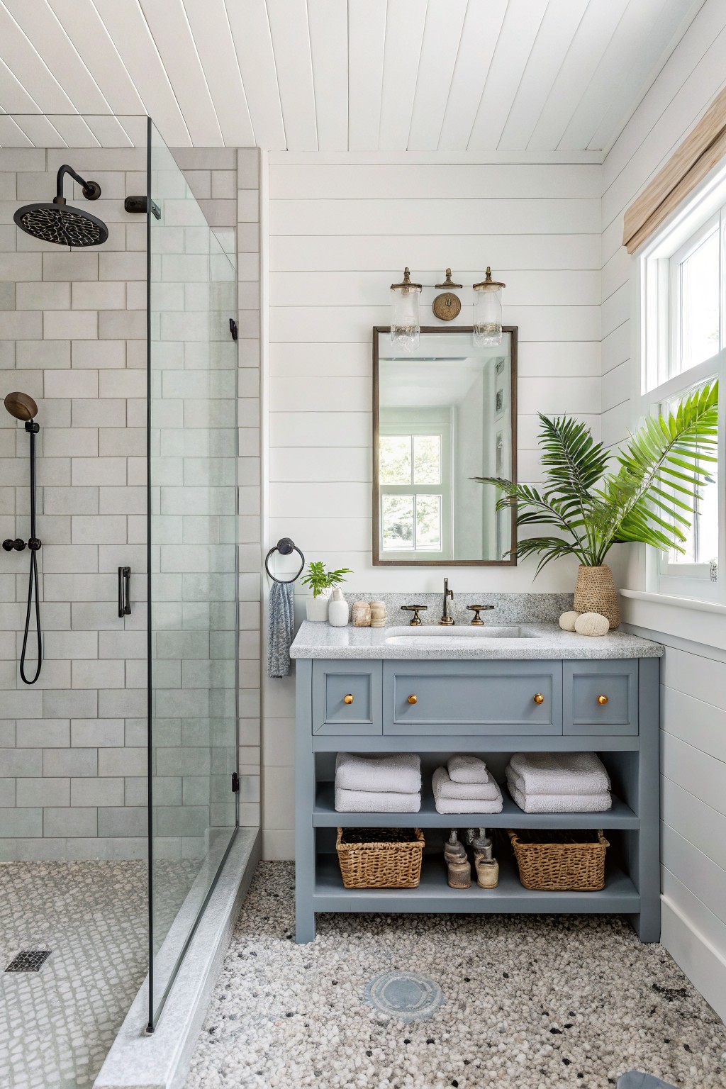A bathroom interior with a soft gray vanity cabinet, white marble countertop, large mirror with three sconces, white shiplap walls, and an adjacent glass-enclosed shower with gray tiles.
