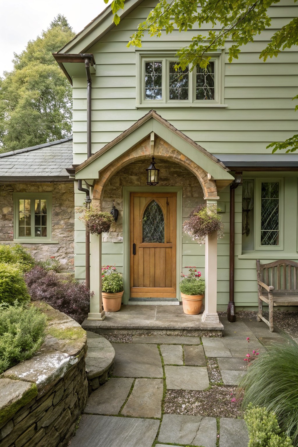 A light green house with a stone arched entry framing a wooden front door and two potted plants on the steps.