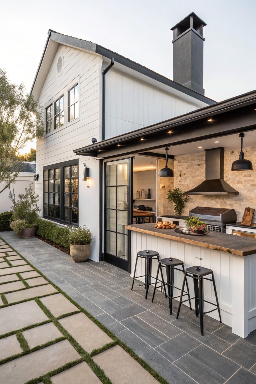 White farmhouse exterior with black trim around windows and doors, plus a covered outdoor kitchen with bar seating.