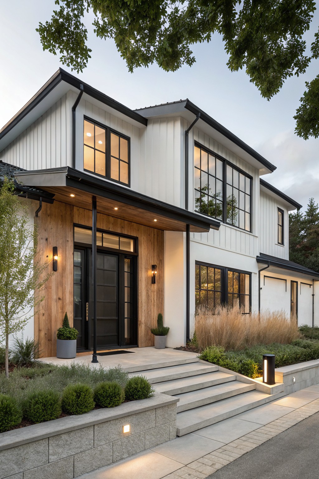 A two-story white house exterior with black trim on windows and doors, a wood-clad entry porch, and concrete steps bordered by low shrubs.