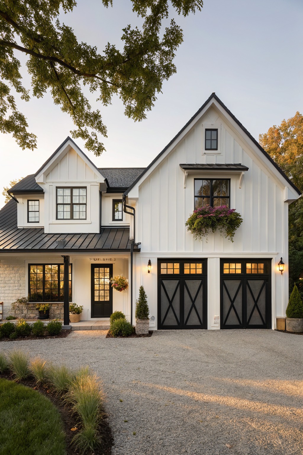 A white two-story farmhouse with black trim, black garage doors, and black window frames, featuring a gravel driveway and landscaping in the foreground.
