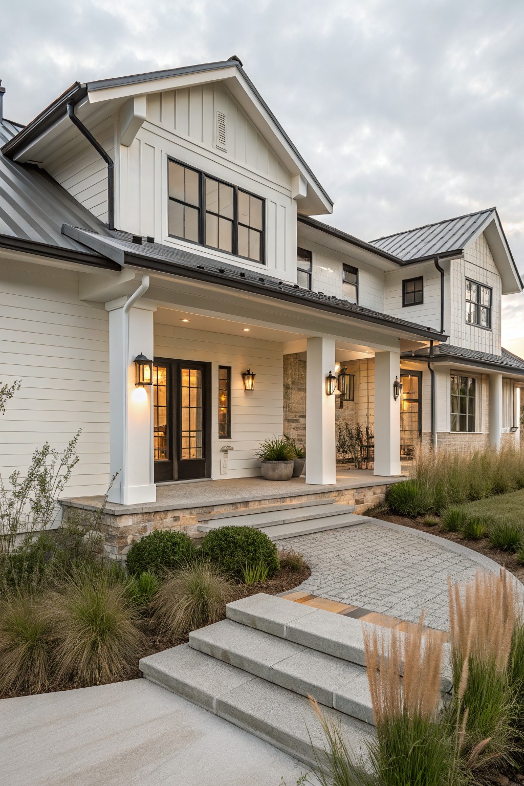 Front view of a white farmhouse ranch home with a covered porch supported by white columns, dark double doors, stone foundation steps, and a paved walkway.