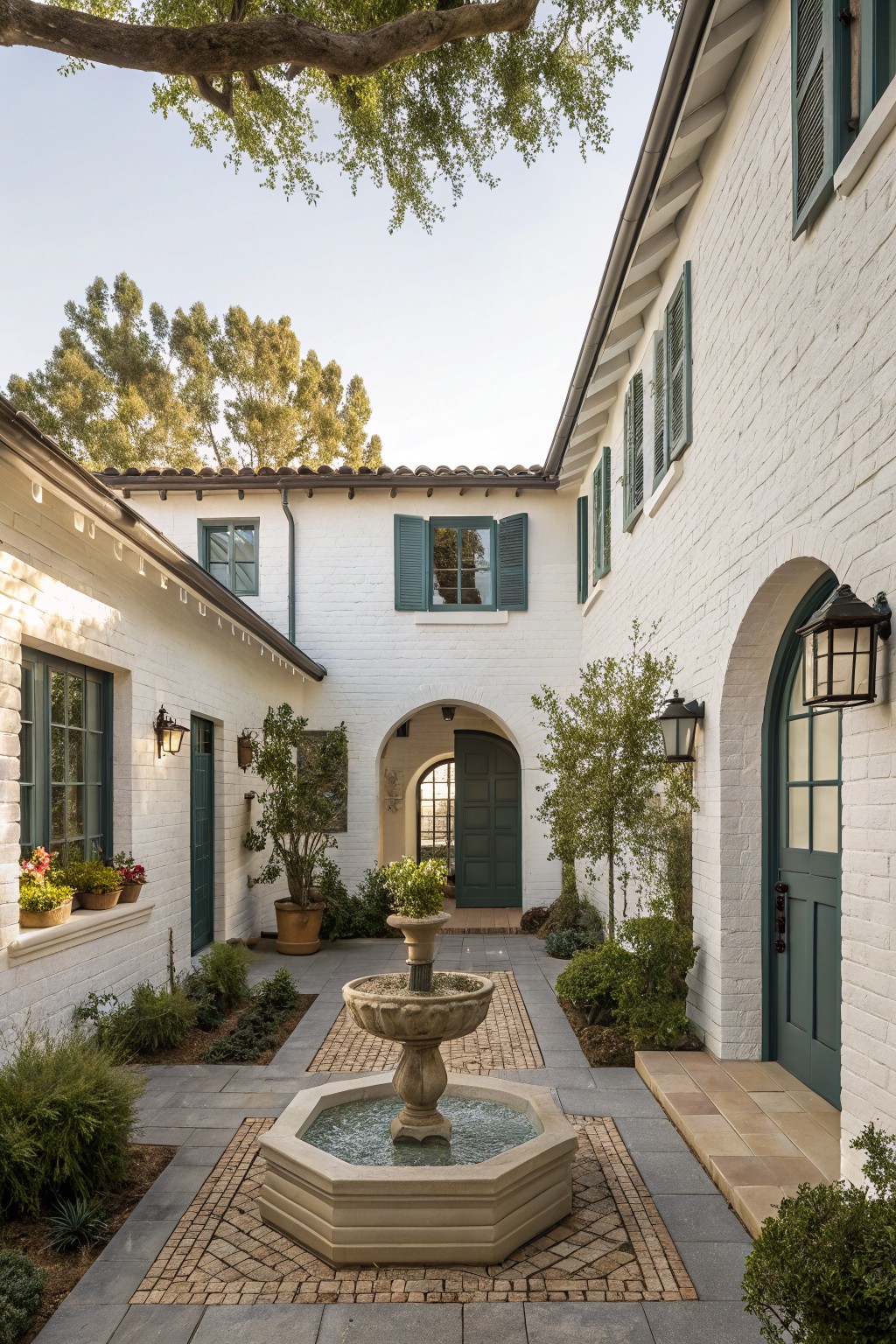 A white brick courtyard with a central stone fountain, green shutters and doors, arched openings, and brick paving.