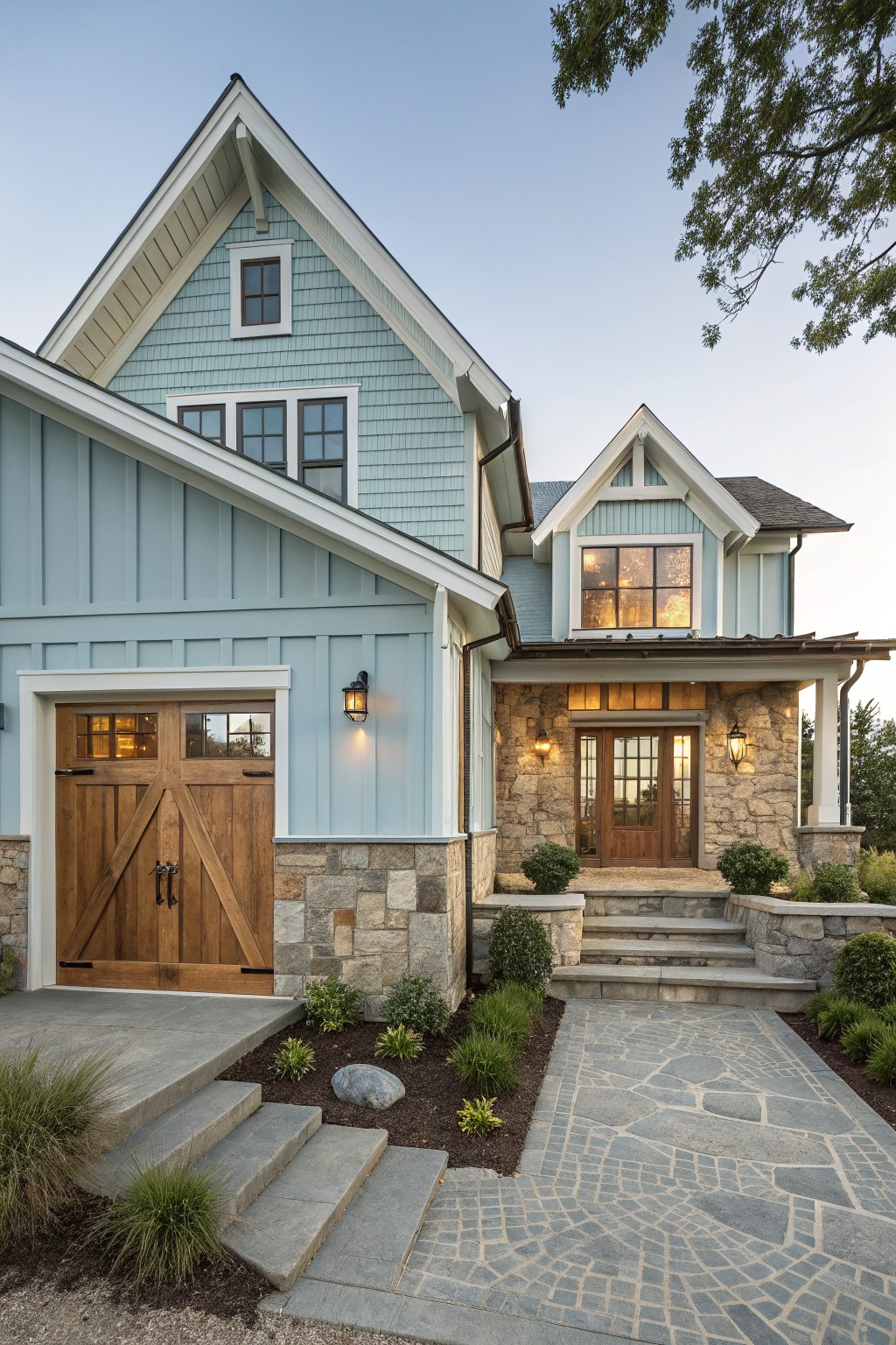 A light blue sided house with white trim, stone foundation and accents, a wooden double garage door on the left, and a covered stone entry porch with steps on the right.