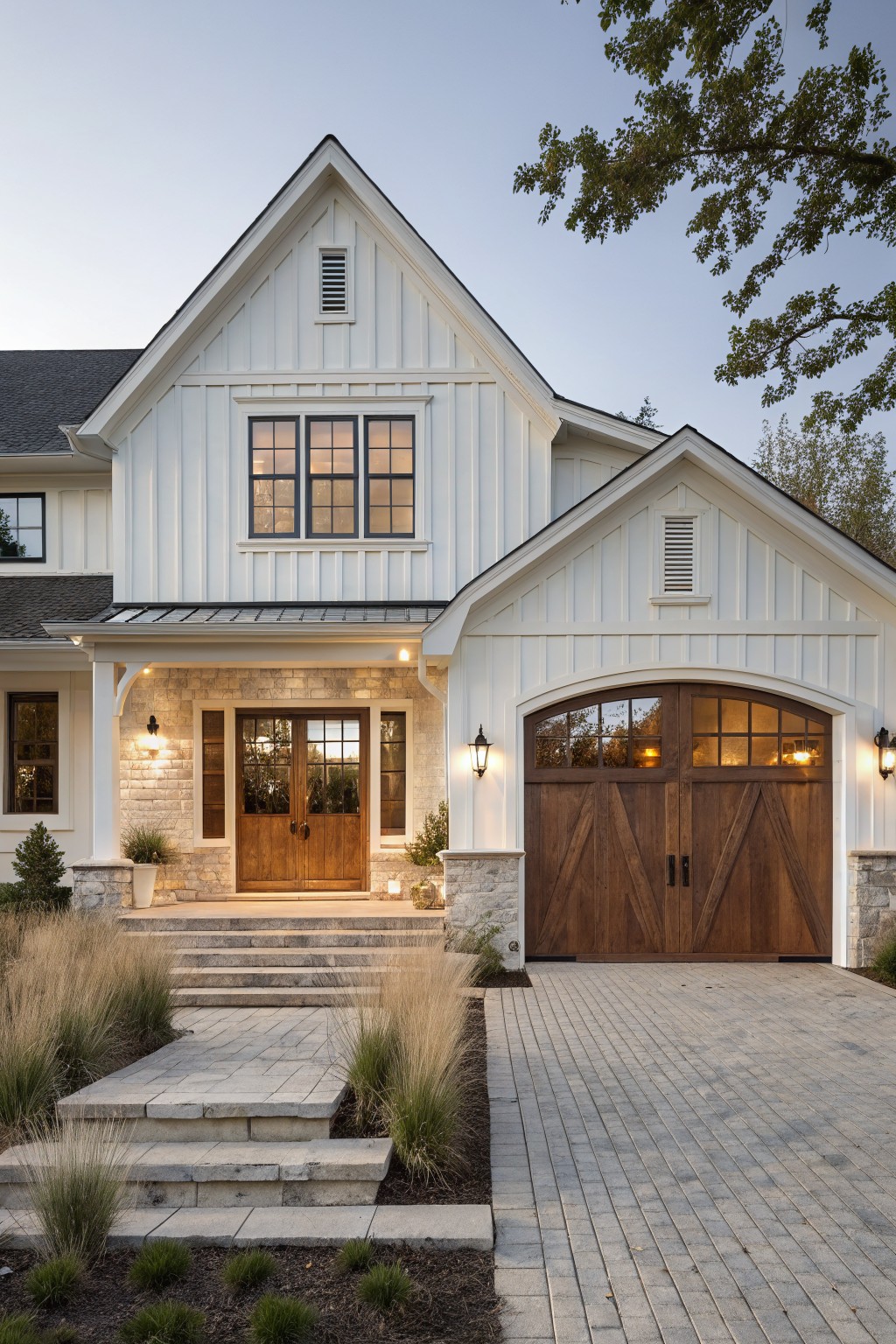 White two-story home with wooden doors, arched garage, stone accents, and steps at dusk