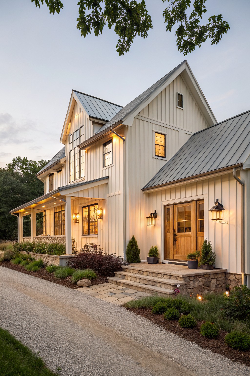 White modern farmhouse with metal roof, lit windows, and stone porch steps at dusk