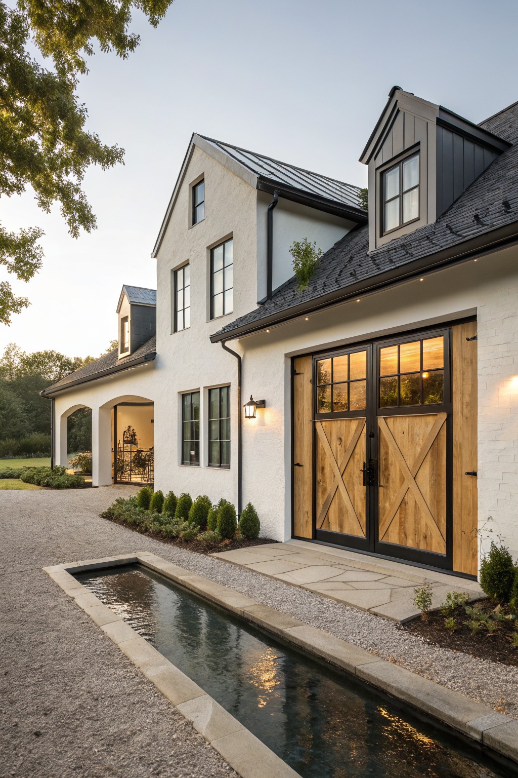 Modern white house with wooden barn doors, dark roof, and reflecting water channel