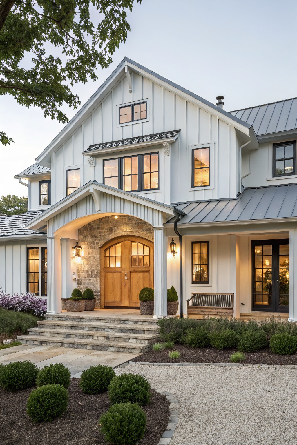 A white modern farmhouse with a large stone arch framing a wooden front door, steps leading up, and landscaping along the front.