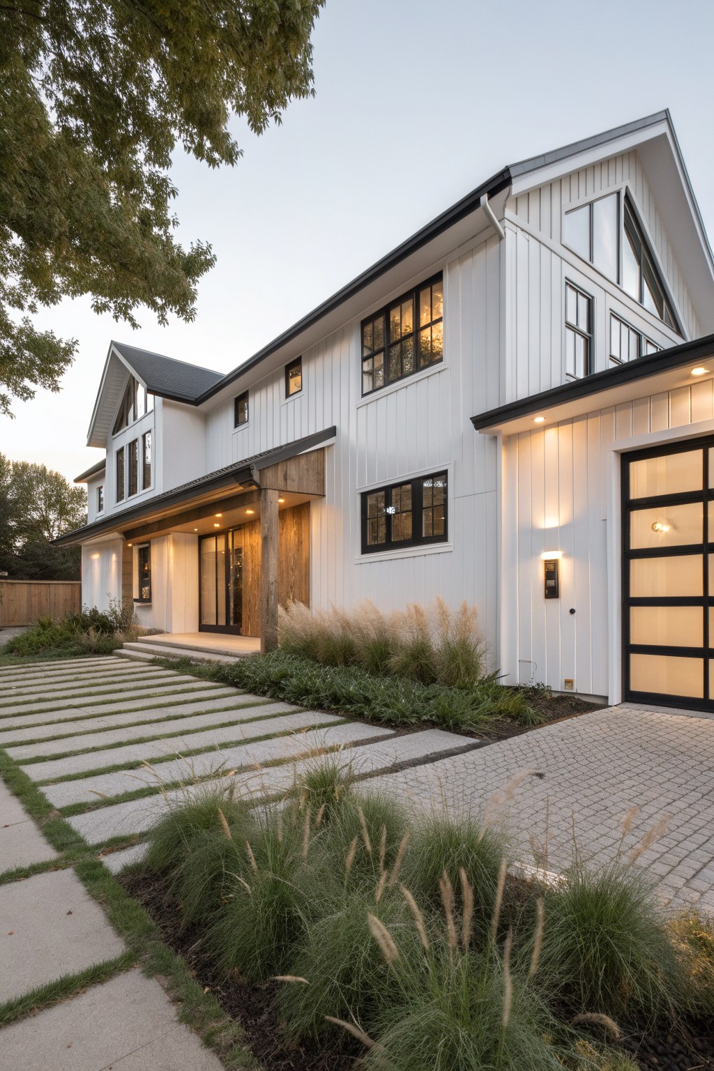 A two-story modern white farmhouse with vertical siding, black-framed windows, wood accents at the entry, and a paved driveway bordered by grasses.
