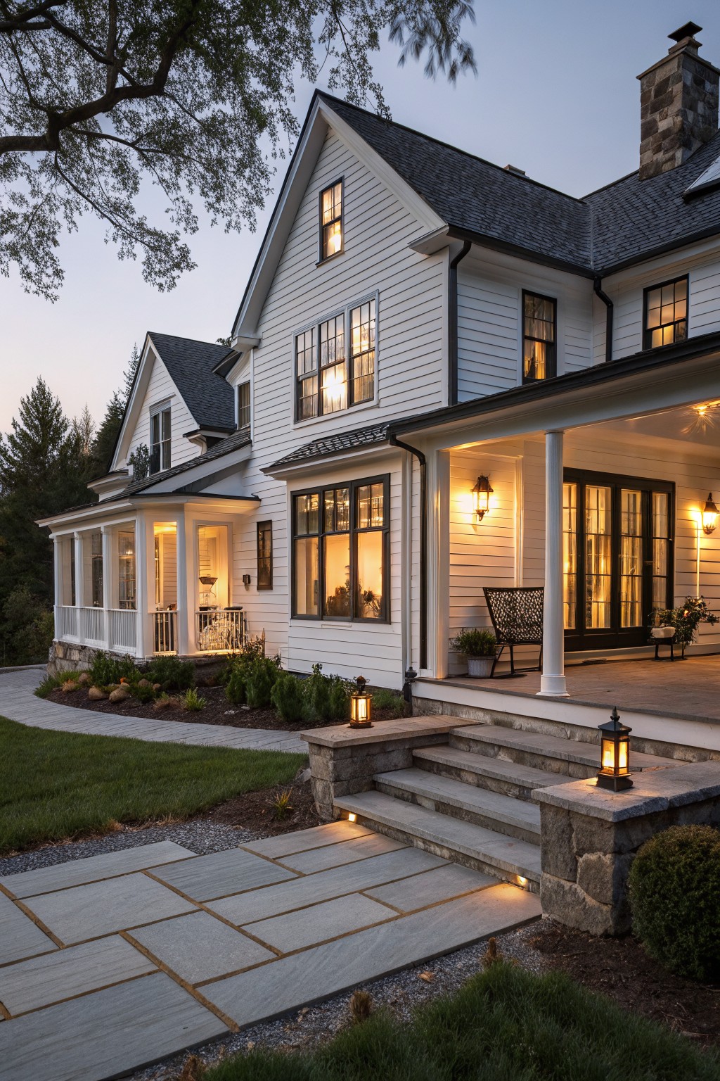 White clapboard house with glowing windows, lit porch, and stone steps at dusk