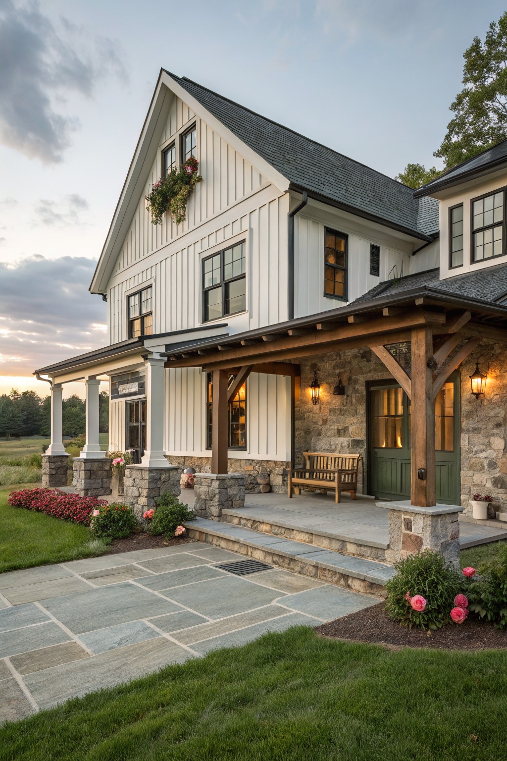 White two-story house with stone base, wooden porch, green door, and stone patio with flowers.